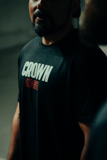 Person wearing a black t-shirt with 'CROWN' printed on it against a dark background